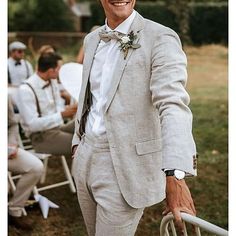 a man in a suit and bow tie standing next to other men sitting on lawn chairs