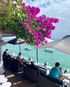 people sitting at tables with umbrellas and flowers on the beach in front of them