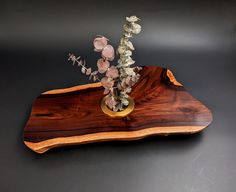 a vase with flowers in it sitting on a wooden tray that is shaped like a piece of wood