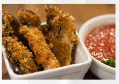 some fried food is in a white bowl next to a small bowl of dipping sauce