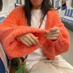 a woman in an orange sweater sitting on a train