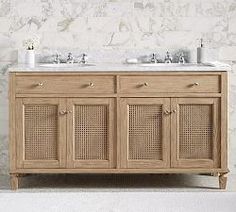 a bathroom vanity with two sinks and wicker doors on the front, against a white marble wall