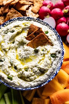 a bowl of dip surrounded by crackers, celery and radishes