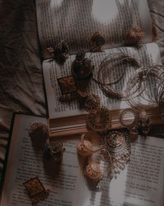 an open book with jewelry laying on top of it next to some candles and rings