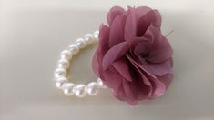 a single pink flower on a white surface next to a pearl beaded bracelet with pearls