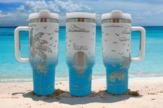 three blue and white travel mugs sitting on the beach