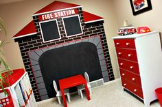 a fire station themed nursery room with red furniture and toys on the floor, along with a chalkboard fireplace