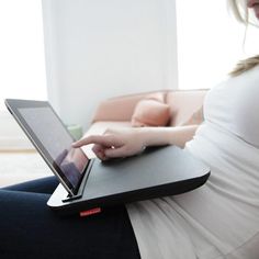 a pregnant woman sitting on a couch with her laptop in her lap and looking at the screen