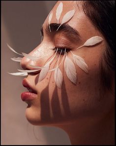 a woman with white feathers painted on her face and eyebrows, looking to the side