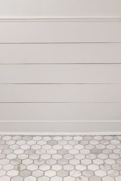 a bathroom with white walls and hexagonal floor tiles on the floor, along with a toilet in the corner