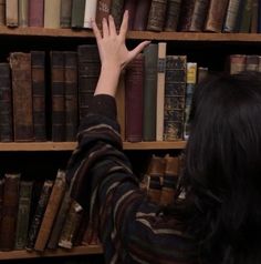 a person reaching for a book on a bookshelf with lots of books behind them