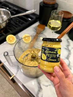 a person holding a jar of lemon pesto sauce in front of a stove top