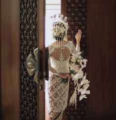 a woman standing in front of a wooden door holding a bouquet of flowers and wearing a wedding dress