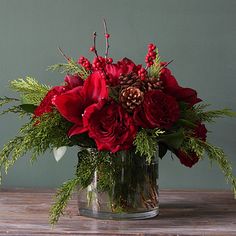 a glass vase filled with red flowers and greenery on top of a wooden table