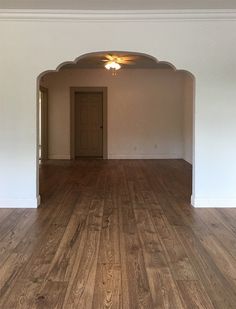 an empty living room with hard wood flooring and arched doorway leading into another room