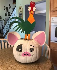 a pumpkin decorated with an animal head and a rooster on it's back sitting on a kitchen table