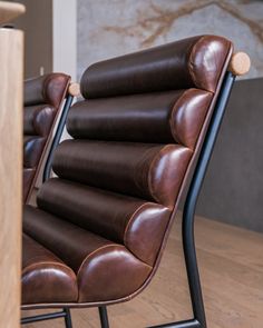 two brown leather chairs sitting next to each other on a wooden floor in front of a wall