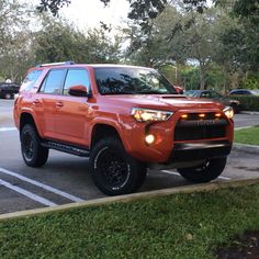 an orange toyota 4runner is parked in a parking lot with other cars behind it