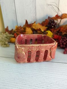 a pink bracelet sitting on top of a white table next to some grapes and leaves