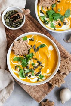 two bowls filled with carrot soup and topped with toasted pumpkin seeds, green leafy garnishments