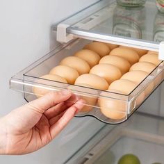 an open refrigerator door with eggs in the bottom drawer and one being held by someone's hand