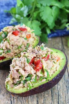 an avocado filled with tuna salad on top of a wooden table next to other food