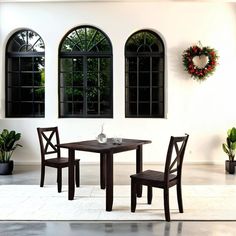 two chairs and a table in front of three windows with wreaths on the wall