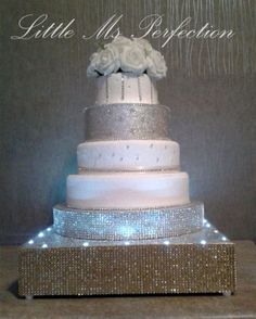 a three tiered wedding cake with white flowers and sparkles on the bottom layer