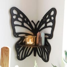 a butterfly shaped candle holder on a wall next to a potted plant and some candles