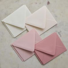 four envelopes are lined up on a marble counter top, one is pink and the other is white