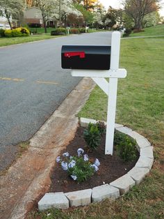 a white mailbox sitting on the side of a road next to a flower bed