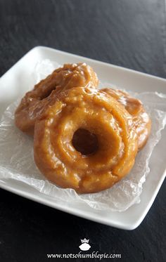 two glazed donuts sitting on top of a white square plate with plastic wrapper