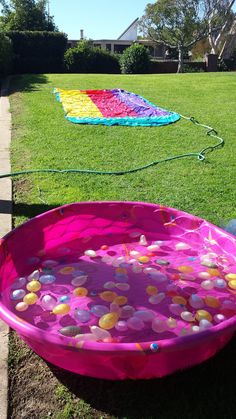 a pink plastic tub filled with lots of candy on top of a lush green field