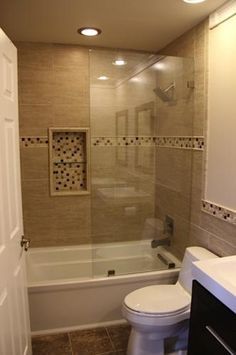 a white toilet sitting next to a bath tub under a bathroom mirror with lights on