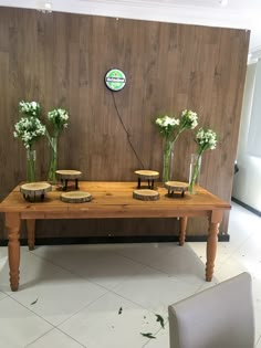 a wooden table topped with vases filled with flowers next to a wall mounted clock