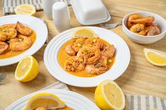 two white plates topped with shrimp next to lemon wedges