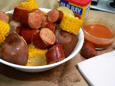 a white bowl filled with hot dogs and corn on the cob next to a container of sauce