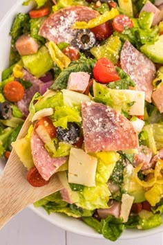 a salad with ham, lettuce, tomatoes and other toppings in a white bowl