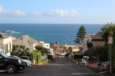 cars parked on the side of a road next to houses near the ocean and water