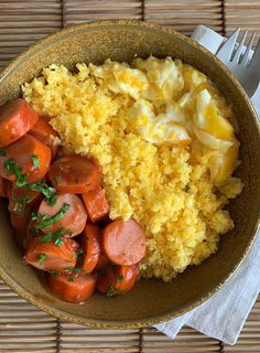 a bowl filled with rice and sausage next to a fork on top of a table