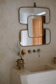 a bathroom sink sitting under a large mirror next to a vase with flowers in it