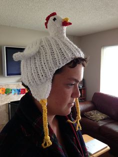 a woman wearing a knitted chicken hat in front of a couch with a window