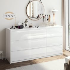 a white dresser sitting next to a window with a round mirror on top of it