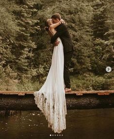 a bride and groom kissing on a bridge over a river in front of some trees