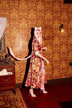 a woman with pink hair wearing a red and gold dress standing in front of a wall