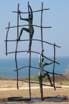 two statues made out of sticks and rope in front of the ocean, one standing on its back legs