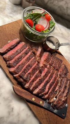 sliced steak on cutting board with salad in bowl