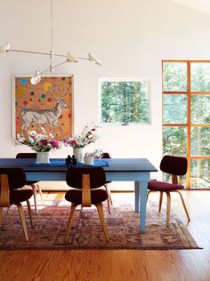 a dining room table with chairs and vases on it in front of a painting