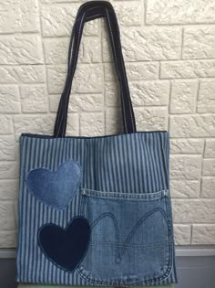 a denim bag with two heart patches on the front and back pocket, hanging against a white brick wall