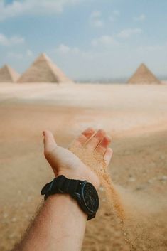 a hand holding sand in front of three pyramids